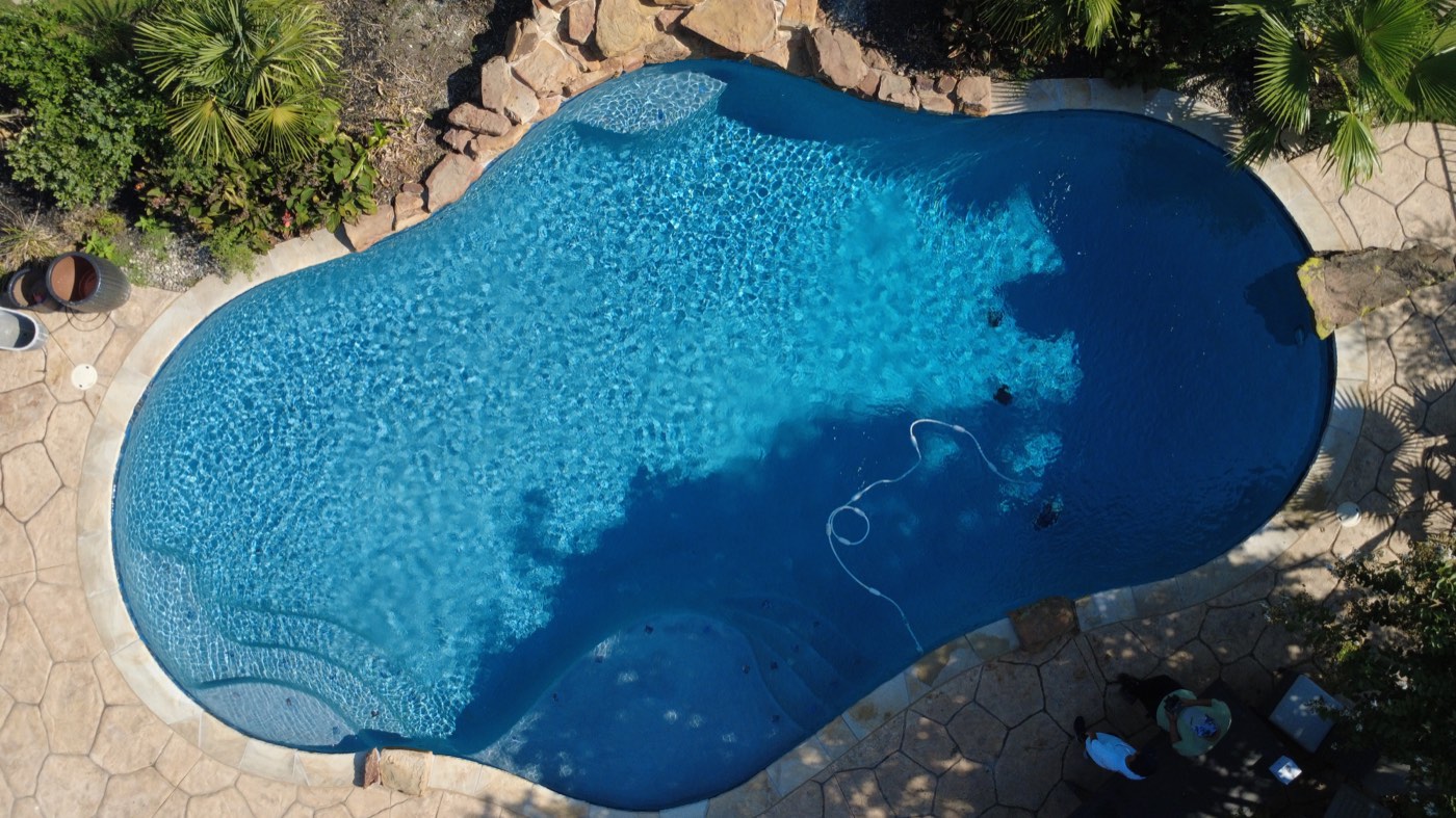 Aerial view of a renovated freeform pool with new tile, stone coping and deck